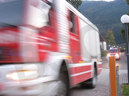 Dynamische Fotoaufnahme eines gerade ankommenden und durch die Geschwindigkeit am Foto verschwommen dargestellten Feuerwehr-Löschfahrzeugs und dahinter einem Mannschaftstransportfahrzeugs im Rahmen ei