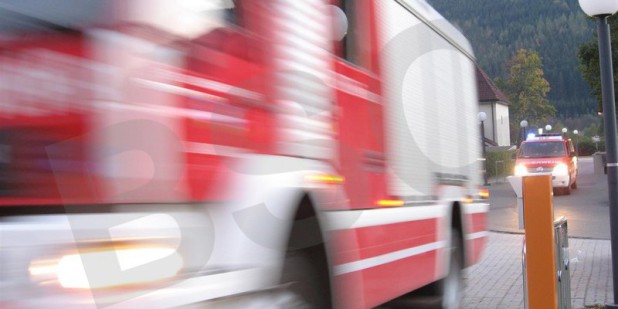 Dynamische Fotoaufnahme eines gerade ankommenden und durch die Geschwindigkeit am Foto verschwommen dargestellten Feuerwehr-Löschfahrzeugs und dahinter einem Mannschaftstransportfahrzeugs im Rahmen ei